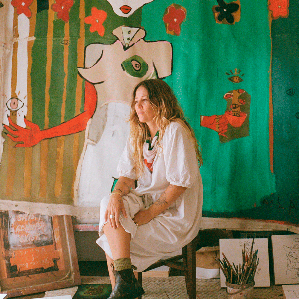 Karlee Mackie sitting in front of a colourful abstract painting in an art studio.