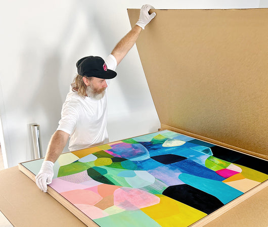 A person packing a bright, colourful artwork in a large box